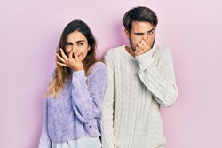 Young hispanic couple wearing casual clothes smelling something stinky and disgusting, intolerable smell, holding breath with fingers on nose. bad smell 