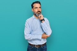 Middle aged man with beard wearing business shirt with hand on chin thinking about question, pensive expression. smiling and thoughtful face. doubt concept. 