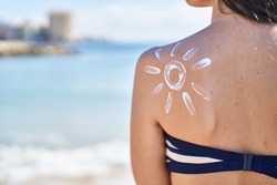 Young hispanic woman wearing bikini standing with sun lotion on back at seaside