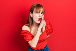 Redhead young woman wearing casual red t shirt hand on mouth telling secret rumor, whispering malicious talk conversation 