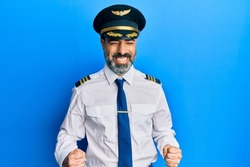 Middle age man with beard and grey hair wearing airplane pilot uniform excited for success with arms raised and eyes closed celebrating victory smiling. winner concept. 