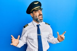 Middle age man with beard and grey hair wearing airplane pilot uniform crazy and mad shouting and yelling with aggressive expression and arms raised. frustration concept. 