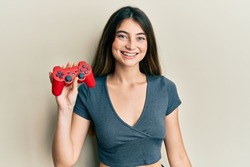 Young caucasian woman playing video game holding controller looking positive and happy standing and smiling with a confident smile showing teeth 