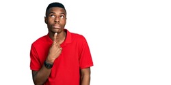 Young african american man wearing casual red t shirt thinking concentrated about doubt with finger on chin and looking up wondering 