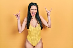 Young hispanic girl wearing swimsuit shouting with crazy expression doing rock symbol with hands up. music star. heavy music concept. 