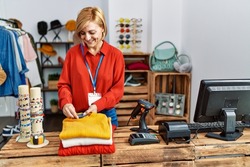 Middle age blonde woman smiling confident holding alarm clothes at clothing store