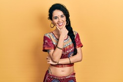 Young woman wearing bindi and bollywood clothing looking confident at the camera smiling with crossed arms and hand raised on chin. thinking positive. 