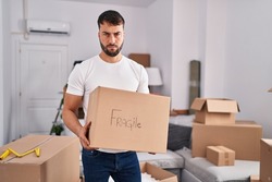 Handsome hispanic man moving to a new home holding fragile box depressed and worry for distress, crying angry and afraid. sad expression. 