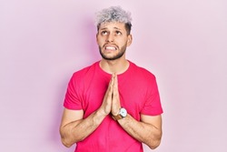 Young hispanic man with modern dyed hair wearing casual pink t shirt begging and praying with hands together with hope expression on face very emotional and worried. begging. 