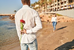 Man and woman couple surprise with rose on back at seaside