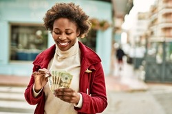 Young african american woman holding dollar bank notes at the city