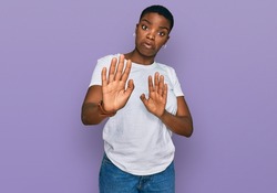 Young african american woman wearing casual white t shirt moving away hands palms showing refusal and denial with afraid and disgusting expression. stop and forbidden. 