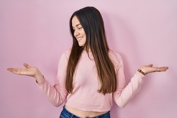 Young brunette woman standing over pink background smiling showing both hands open palms, presenting and advertising comparison and balance 