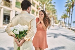 Man and woman having anniversary surprise holding bouquet of flowers at seaside