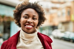 Beautiful business african american woman with afro hair smiling happy and confident outdoors at the city