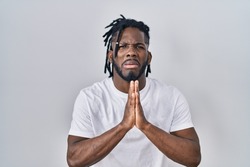 African man with dreadlocks wearing casual t shirt over white background begging and praying with hands together with hope expression on face very emotional and worried. begging. 