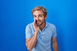 Caucasian man standing over blue background hand on mouth telling secret rumor, whispering malicious talk conversation 