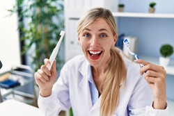Beautiful dentist woman holding ordinary toothbrush and electric toothbrush smiling and laughing hard out loud because funny crazy joke. 