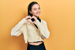 Young brunette girl wearing casual yellow jacket smiling in love doing heart symbol shape with hands. romantic concept. 