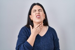 Young brunette woman standing over isolated background touching painful neck, sore throat for flu, clod and infection 