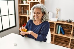 Middle age grey-haired woman taking pills sitting on the table at home.