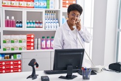 African american woman pharmacist using computer talking on telephone at pharmacy