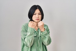 Young asian woman standing over white background ready to fight with fist defense gesture, angry and upset face, afraid of problem 