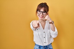 Young beautiful woman wearing casual shirt over yellow background smiling doing talking on the telephone gesture and pointing to you. call me. 