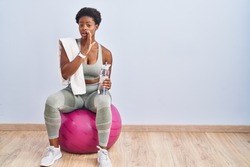 African american woman wearing sportswear sitting on pilates ball hand on mouth telling secret rumor, whispering malicious talk conversation 