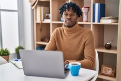 Young african man with dreadlocks working using computer laptop relaxed with serious expression on face. simple and natural looking at the camera. 