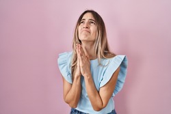 Young hispanic woman standing over pink background begging and praying with hands together with hope expression on face very emotional and worried. begging. 