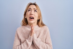 Hispanic woman standing over blue background begging and praying with hands together with hope expression on face very emotional and worried. begging. 