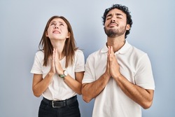 Young couple wearing casual clothes standing together begging and praying with hands together with hope expression on face very emotional and worried. begging. 