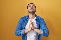 Hispanic man standing over yellow background begging and praying with hands together with hope expression on face very emotional and worried. begging. 