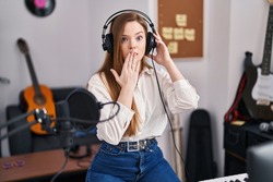 Young caucasian woman recording song at music studio covering mouth with hand, shocked and afraid for mistake. surprised expression 