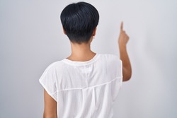 Young asian woman with short hair standing over isolated background posing backwards pointing ahead with finger hand 