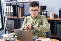 Young non binary man business worker using laptop looking watch at office