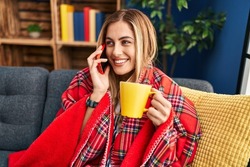 Young blonde woman drinking coffee and talking on the smartphone at home