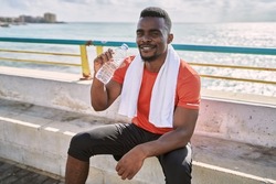Young african american man wearing sportswear holding water bottle at seaside