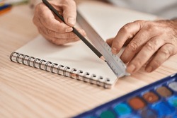 Middle age grey-haired man artist drawing line on notebook using tape measure at laboratory