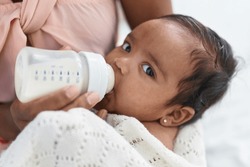 African american baby sucking feeding bottle at bedroom