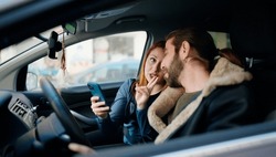 Man and woman couple using smartphone driving car at street