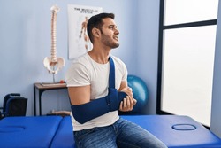 Young hispanic man injured physiotherapy patient suffering for arm pain at rehab clinic