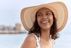 Young african american woman wearing summer hat looking to the side at seaside