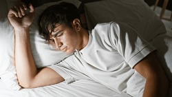 Exhausted young hispanic man finds comfort in a bright morning sleep, lying undisturbed in his cozy bedroom, surrendering to the soft embrace of his bed and pillow, in a relaxed indoor portrait.