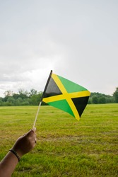 Jamaica hand flag on green meadow. National flag