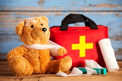 Paediatric healthcare concept with a little teddy bear with its arm in a sling alongside a first aid kit and bandages on rustic wood