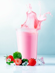 Liquid splashing out of a glass filled with delicious healthy blended strawberry smoothie served with ripe whole fruit