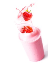 Ripe red fresh strawberries splashing into a glass of blended fruit smoothie with creamy yoghurt