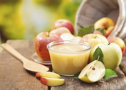 Preparing apple puree or sauce in a small glass jar with sliced apple pieces and a wooden spoon on an old wooden table outdoors